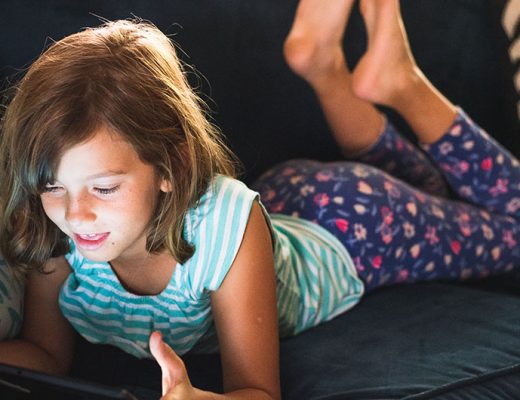 Girl having fun with a tablet on sofa. Screen time controls post on MamiTalks.com