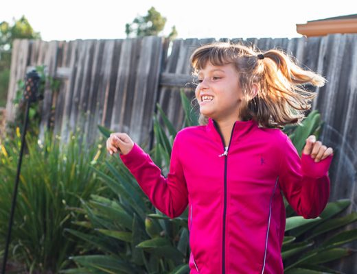 Girl jumping with pink jacket in backyard. Kids on 45th. A new way to shop for kid's clothes.